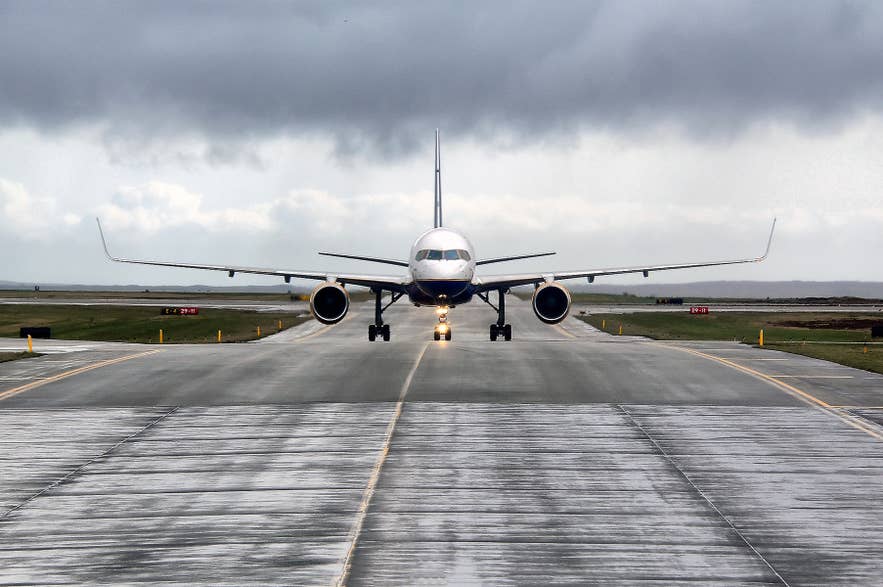 Passenger jet taxis on a wet runway at Keflavik International Airport under cloudy skies in Iceland. Passenger jet taxis on a wet runway at Keflavik International Airport under cloudy skies in Iceland.