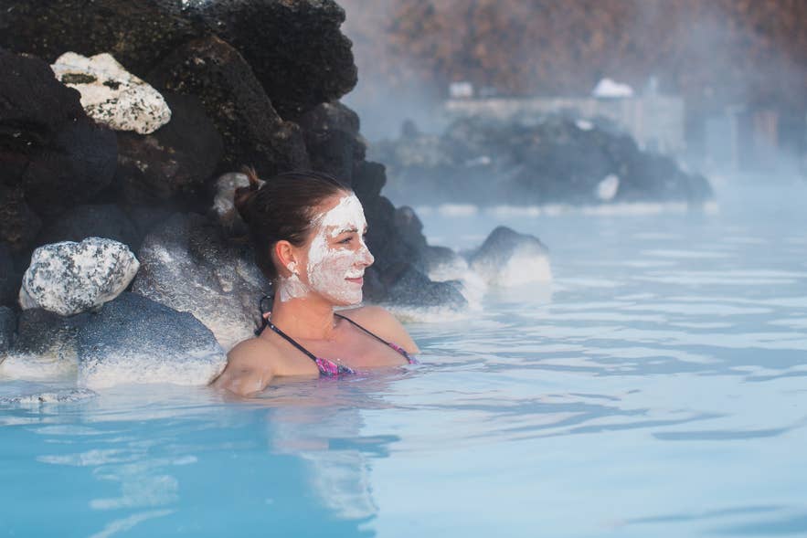 Woman with a silica mud mask relaxes in the milky blue water of Blue Lagoon Geothermal Spa near Keflavik. Woman with a silica mud mask relaxes in the milky blue water of Blue Lagoon Geothermal Spa near Keflavik.