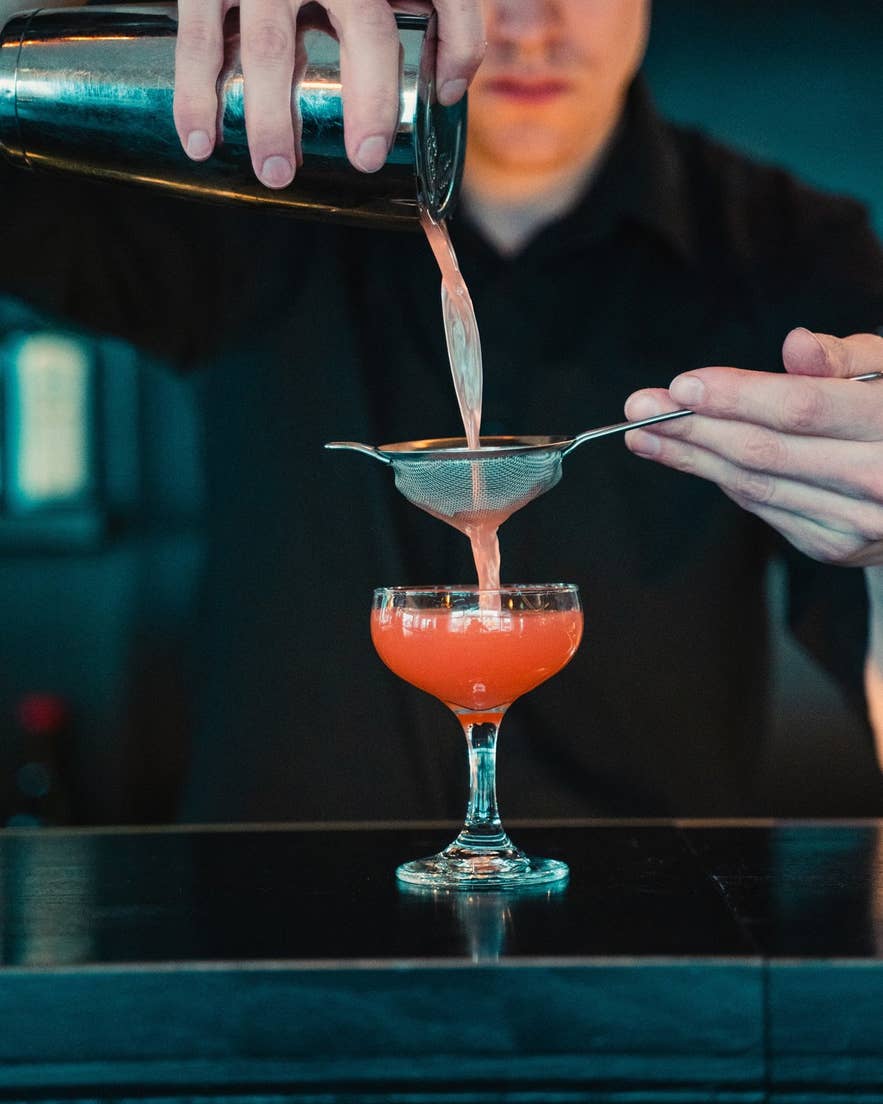 Bartender straining a pink cocktail into a coupe glass at Mulaberg cocktail bar in Akureyri.