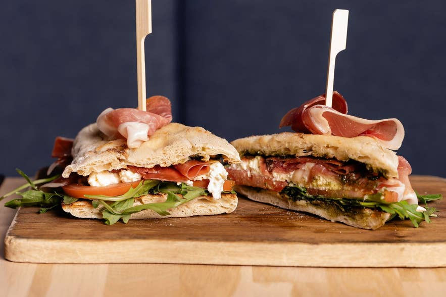 Focaccia sandwiches with cured ham, tomato, and greens on a wooden board at Terian Brasserie