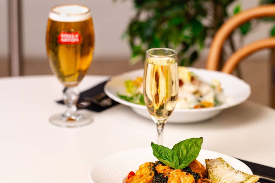 Shrimp pasta, a glass of beer, and sparkling wine on a white table at Terian Brasserie in Akureyri