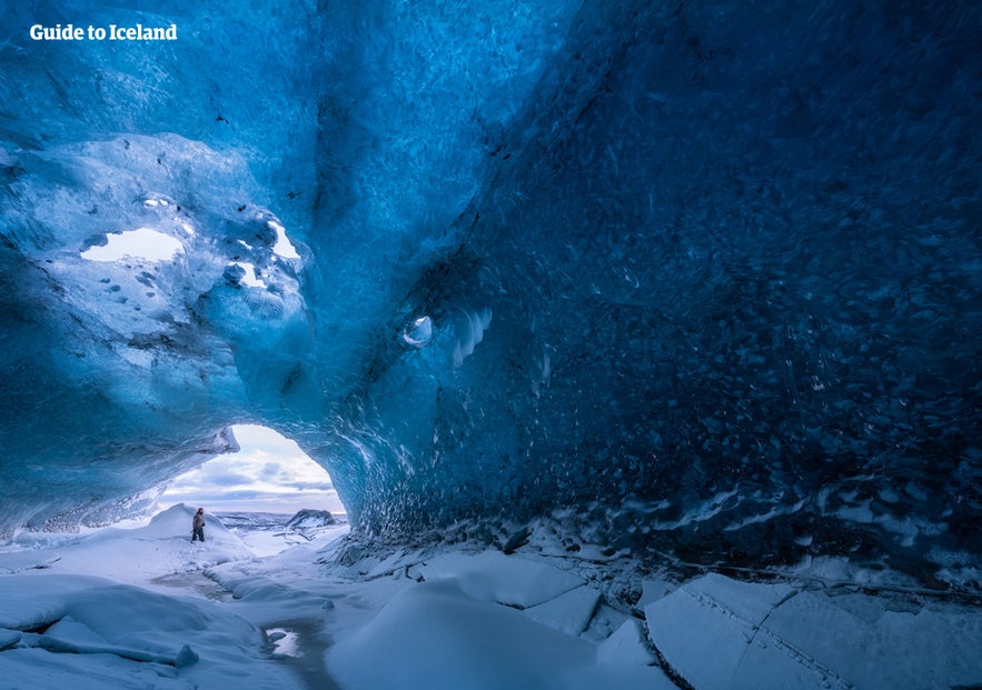 A person standing at the entrance of an Icelandic ice cave with snow inside.