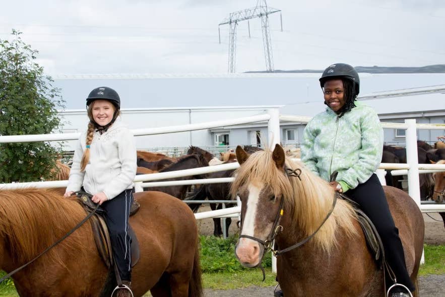 Two children in helmets riding Icelandic horses at a family-friendly stable near Reykjavik.