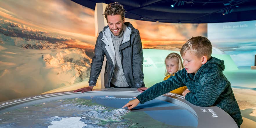 Father and children exploring an interactive glacier exhibit at Perlan, a top indoor attraction for kids.