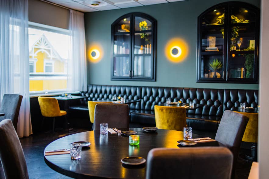 Dining room with green walls, a leather banquette, and yellow velvet chairs at Mulaberg Bistro and Bar in Akureyri.