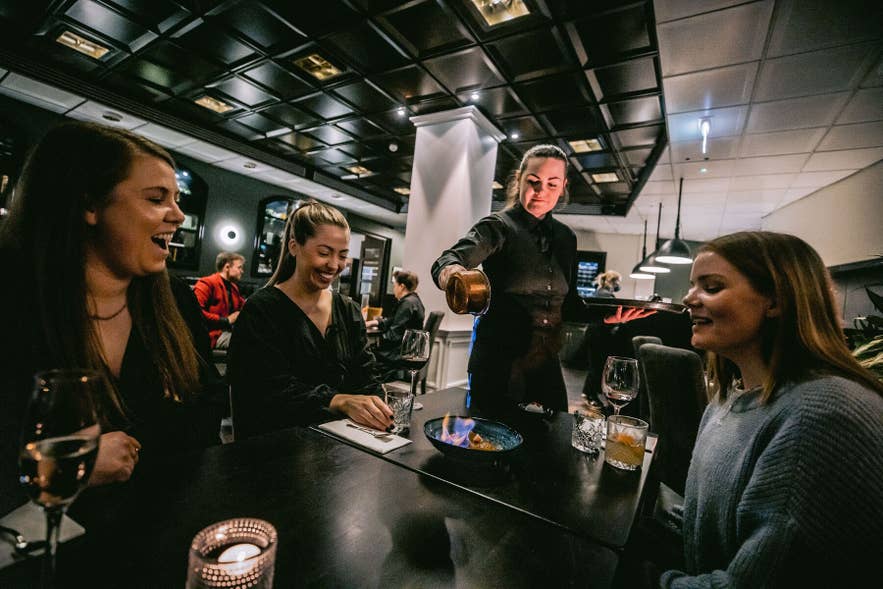 Server pours a flaming dish for guests at the bar inside Mulaberg Bistro and Bar in Akureyri, North Iceland.