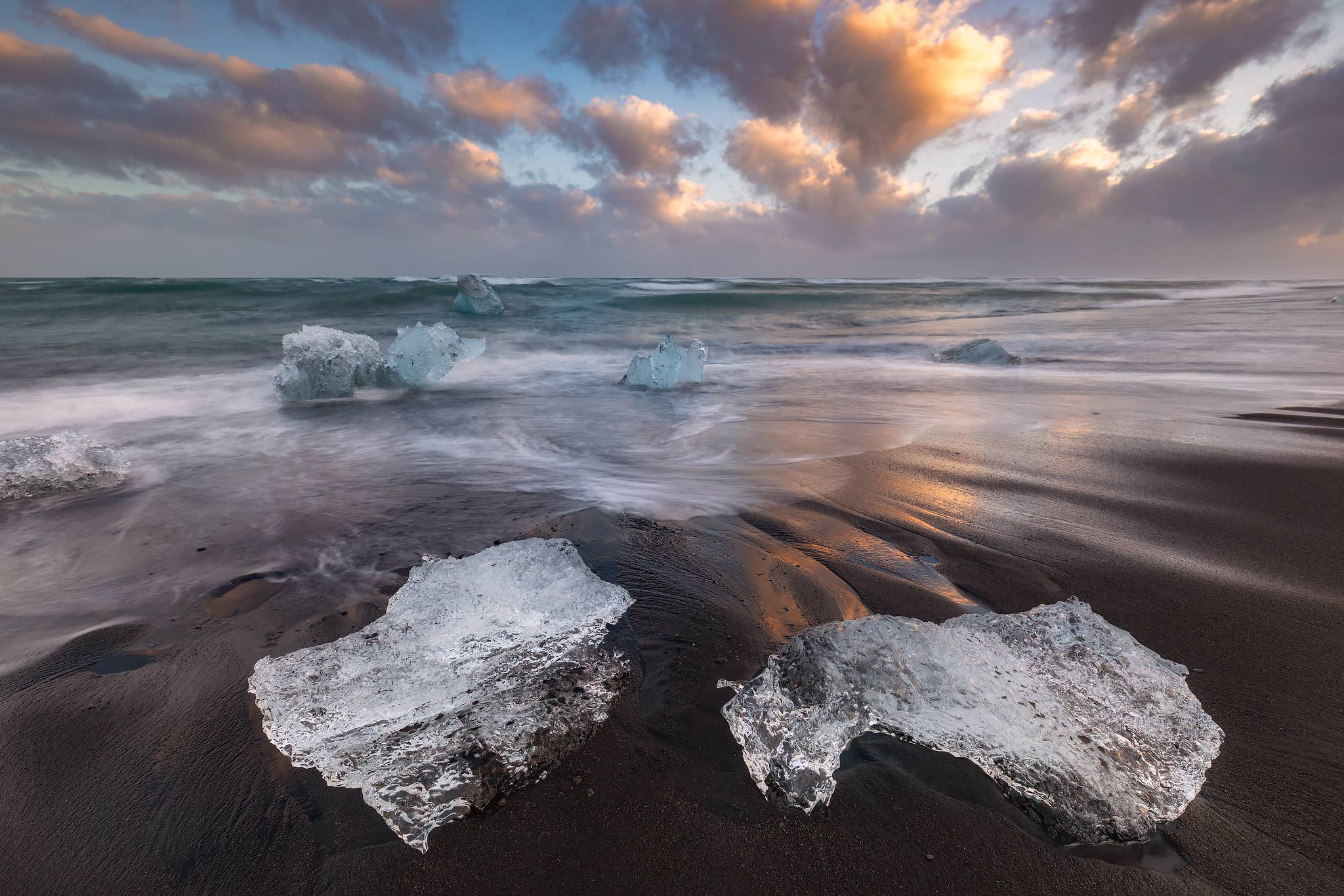 Ice chunks rest on the black sand of Diamond Beach as waves wash ashore near Jokulsarlon Glacier Lagoon.