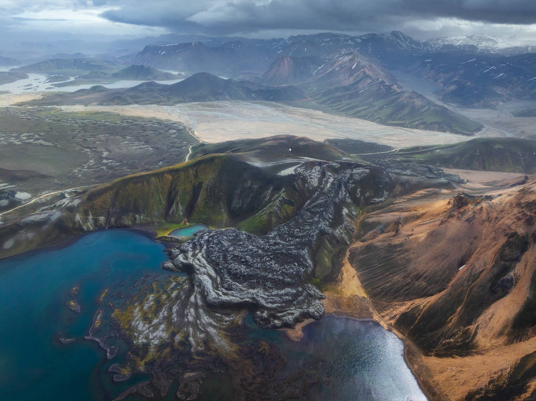 Aerial view of Namshraun Lava Field meeting the blue water of Frostastadavatn Lake near Landmannalaugar.