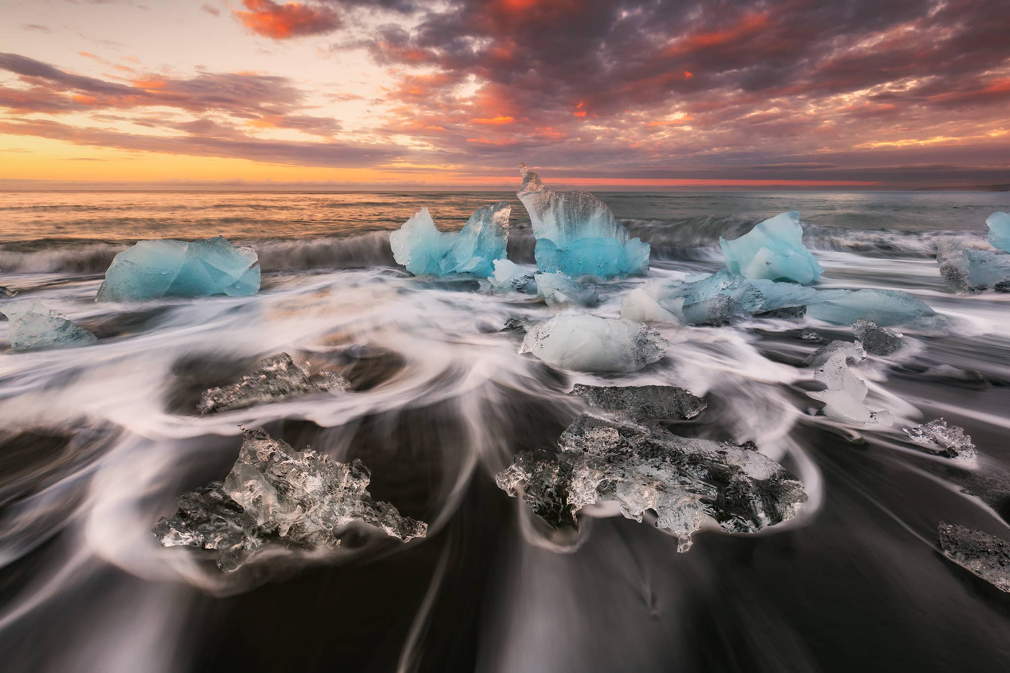 Blue icebergs and clear ice chunks scatter along Diamond Beach at sunset on the South Coast of Iceland.