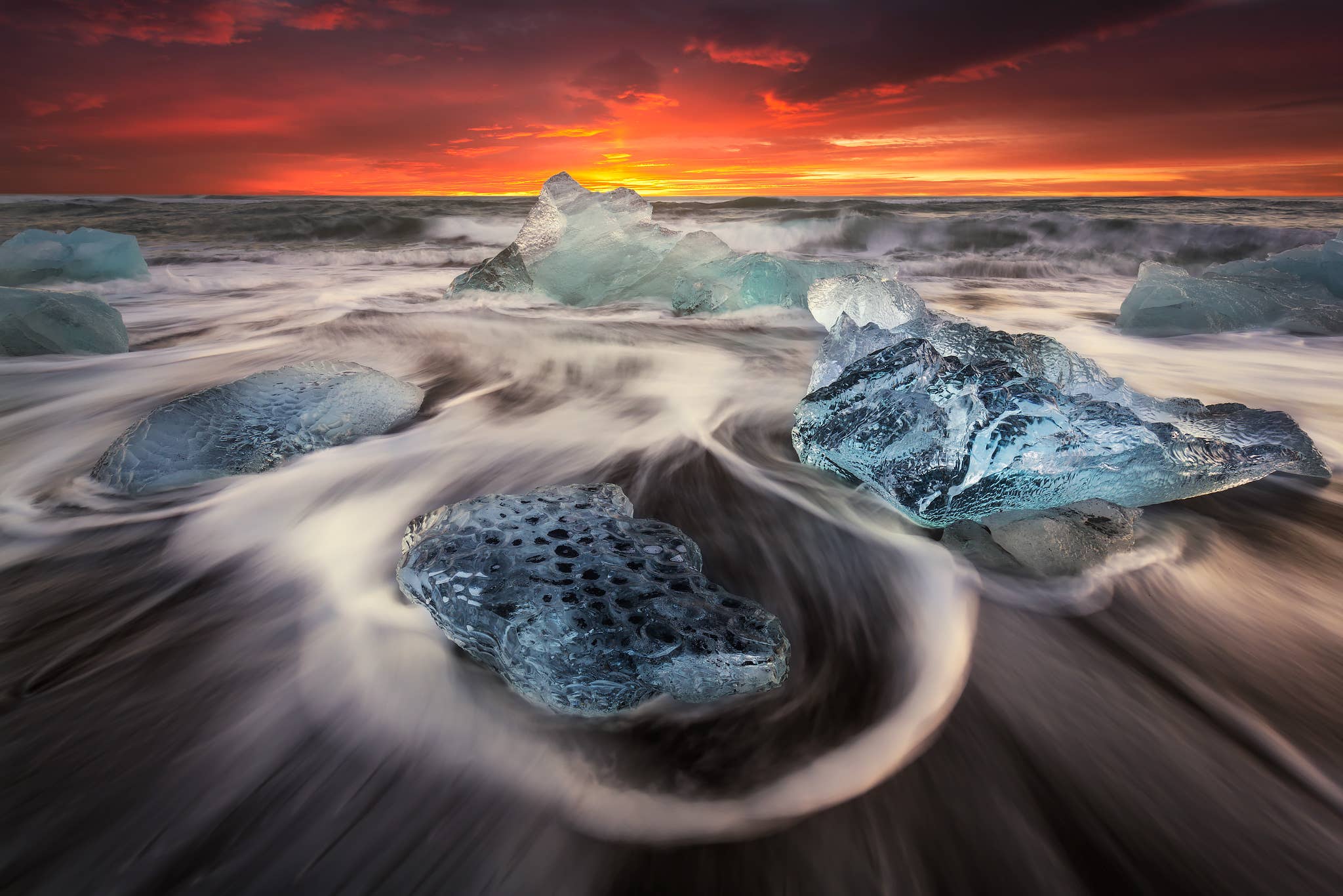 Ocean water swirls around blue icebergs washed up on Diamond Beach near Jokulsarlon Glacier Lagoon.