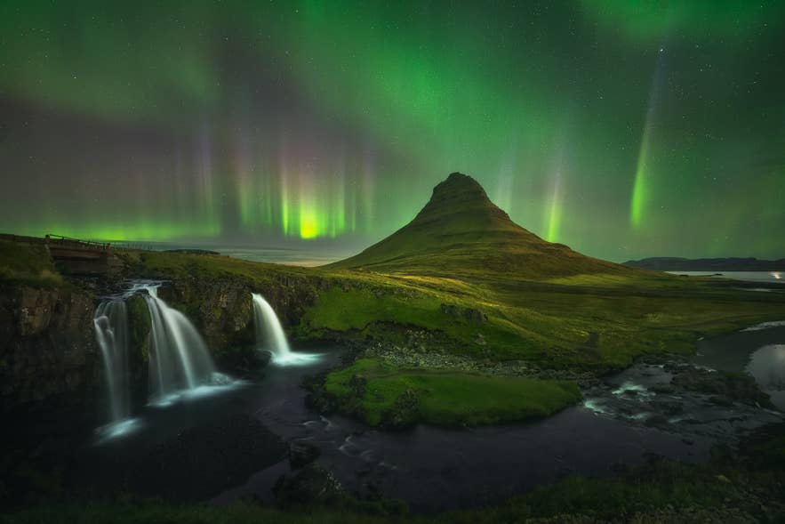 The northern lights glow over Kirkjufell Mountain and Kirkjufellsfoss Waterfall on the Snaefellsnes Peninsula