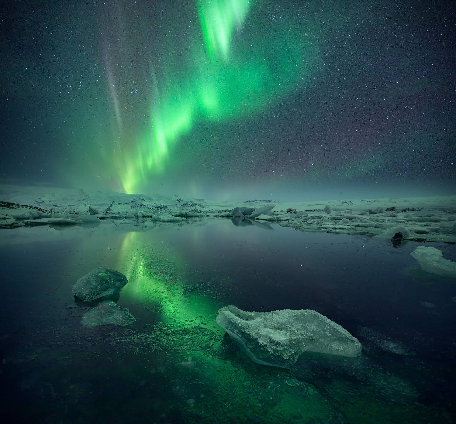 The northern lights reflect in Jokulsarlon Glacier Lagoon among floating icebergs on the South Coast of Iceland.