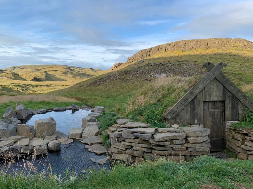 Wooden hut and stone pools at Hrunalaug Hot Spring under a blue sky