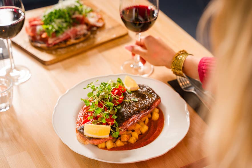 Seared fish fillet with crispy potatoes, cherry tomatoes, and a red sauce, served with red wine at Terian Brasserie in Akureyri