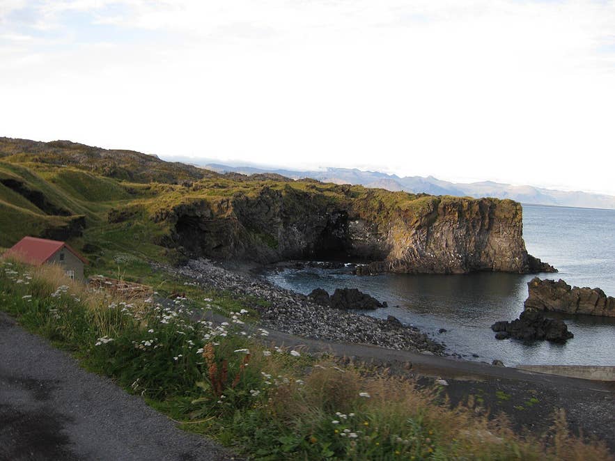 Valasnös headland and the mouth of Baðstofa cave seen across Hellnar cove, with the Fjöruhúsið café