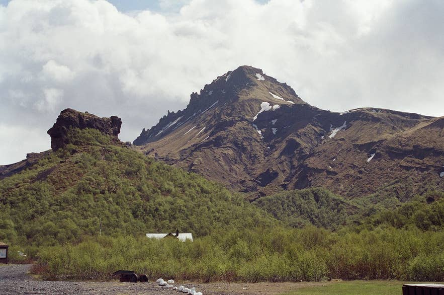 Útigönguhöfði mountain rising above the birch woods and roof of the Básar hut in Goðaland