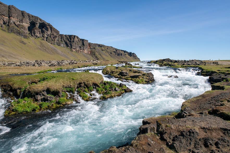 Blue-green rapids of the Fossálar river with the Síða cliffs behind, near Kirkjubæjarklaustur