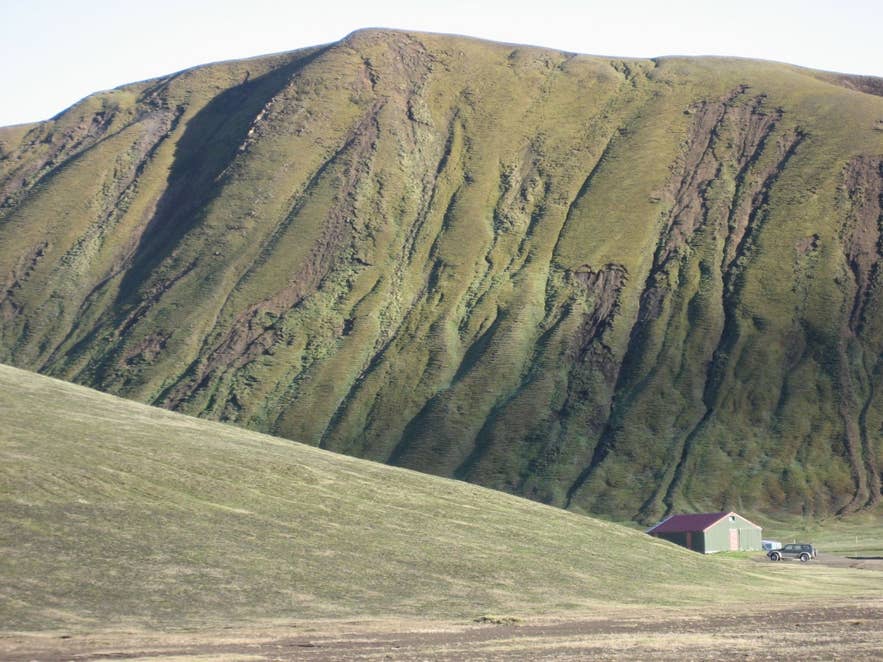 Moss-covered, gully-cut móberg slope of Hellisfjall above a mountain hut at Landmannahellir, Fjallabak
