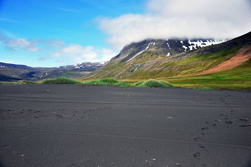 Vöðlavík beach with snow-streaked slopes behind the bay in June Vöðlavík beach with snow-streaked slopes behind the bay in June