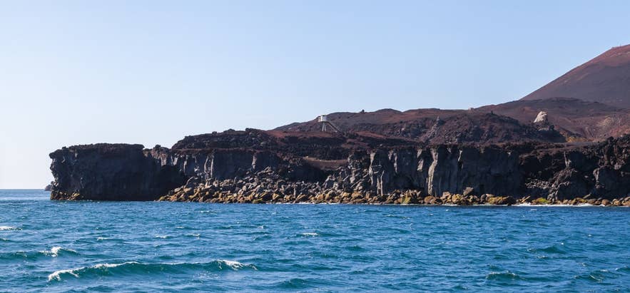 Lava coast at Urðaviti on Heimaey seen from the sea with Eldfell behind Lava coast at Urðaviti on Heimaey seen from the sea with Eldfell behind