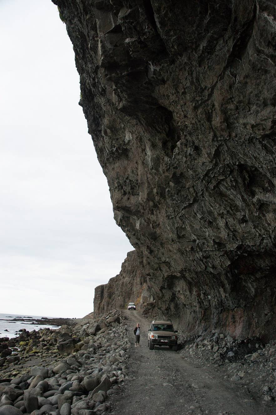 Jeeps driving the boulder beach under the overhanging Skútabjörg cliffs, Arnarfjörður