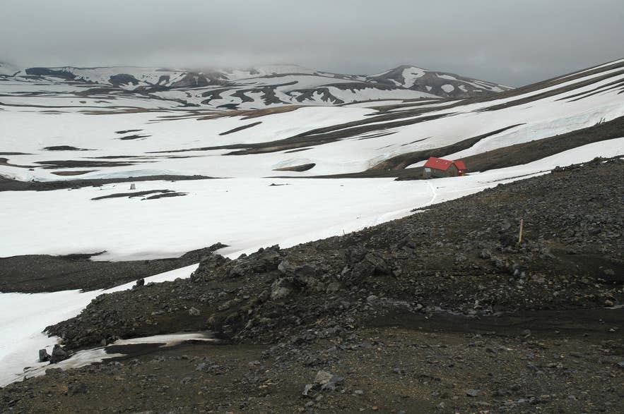 The red-roofed Hrafntinnusker mountain hut among snowfields on the Laugavegur trail south-east of Pokahryggir The red-roofed Hrafntinnusker mountain hut among snowfields on the Laugavegur trail south-east of Pokahryggir