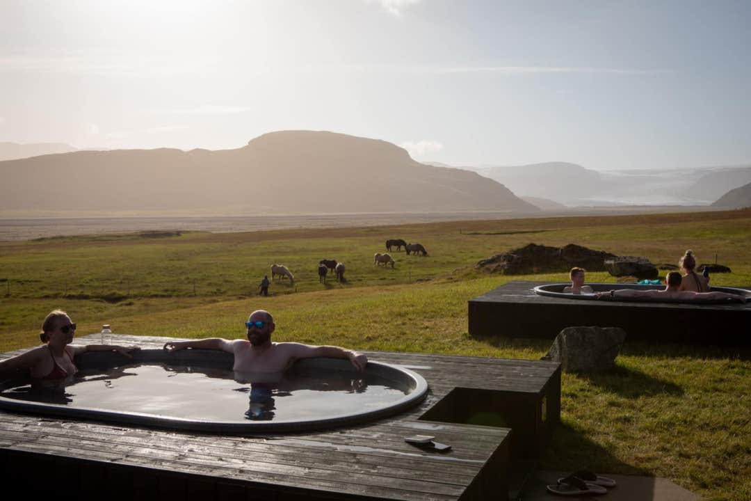 A bather relaxes in a round hot tub at the Hoffell Baths as Icelandic horses graze in the meadow beyond.