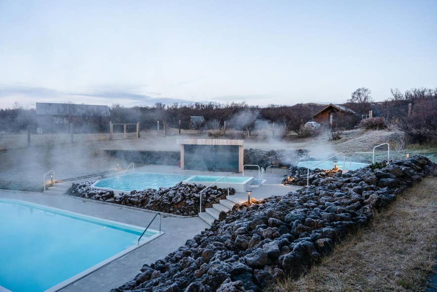 Steam rises from the geothermal pools and lava-rock walls of Lindin at Husafell at dusk.