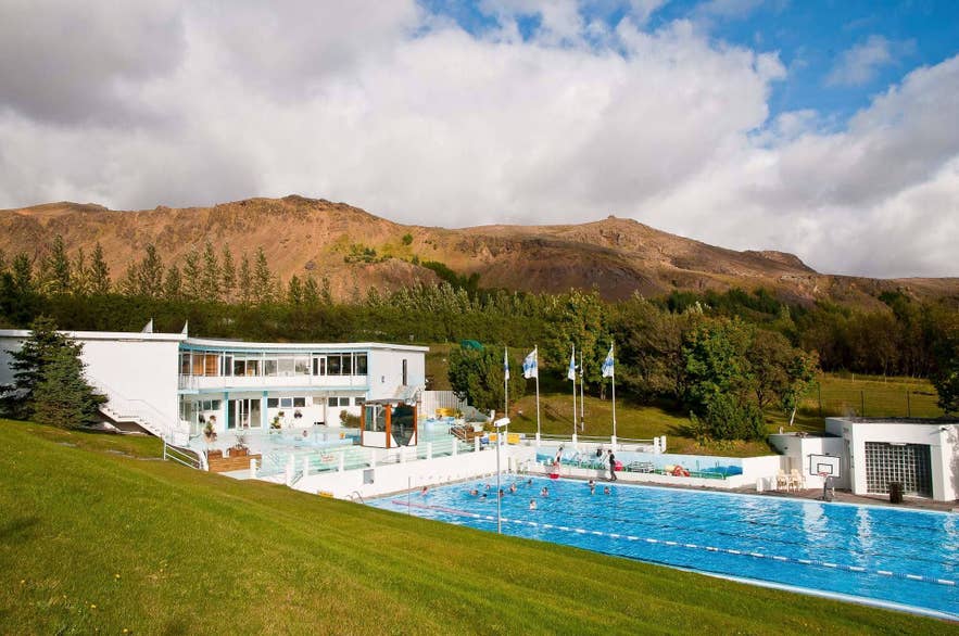 Swimmers in the 50-meter outdoor pool at Laugaskard in Hveragerdi, with hills behind.