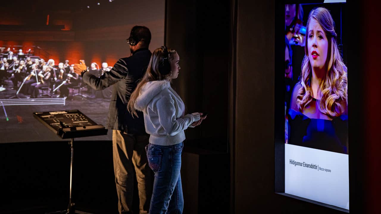 Visitors in audio guide headphones conduct a projected Iceland Symphony Orchestra at the World of Icelandic Music.