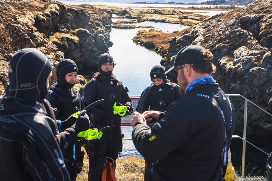 Snorkelers in drysuits listen to their guide at the entry steps of the Silfra fissure in Thingvellir National Park