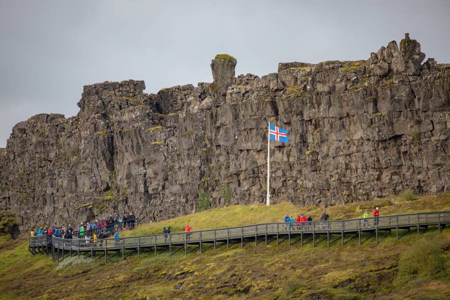 Visitors walking the boardwalk below the Almannagja Gorge cliffs at Thingvellir National Park.