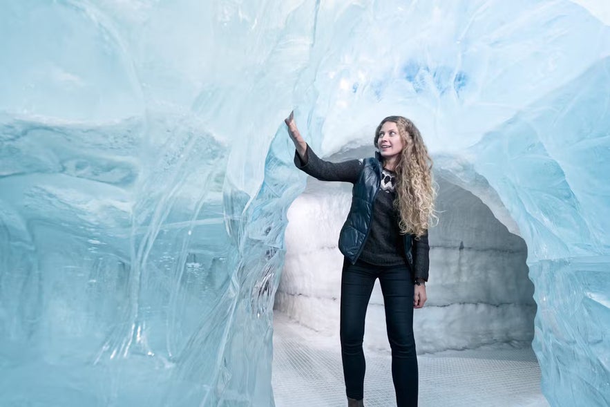 A woman exploring the ice cave installation at Perlan in Reykjavik, touching the icy walls.