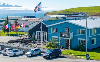 Blue facade of a hotel in Husavik with flags out front and Skjalfandi Bay in the distance in North Iceland.