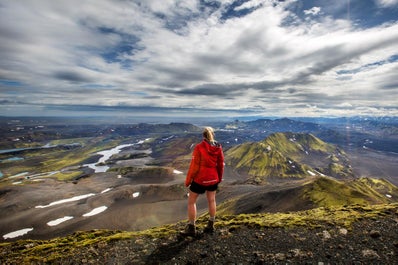 A person stands on a peak overlooking the incredible mountain scenery of the Icelandic Highlands.