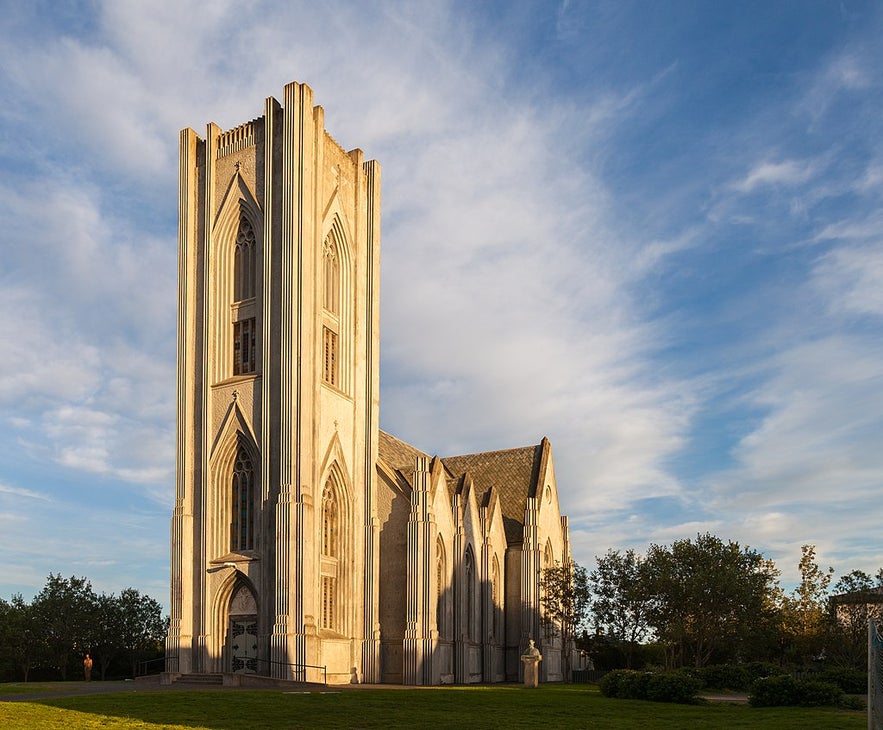 The Landakotskirkja church in Reykjavik, surrounded by grass and with wispy clouds in the blue sky above it.