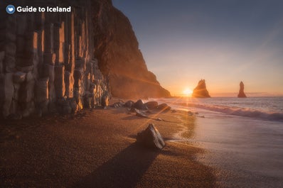 Reynisfjara black sand beach looks stunning at sunset with a warm glow across its jet black sands and dramatic basalt columns.