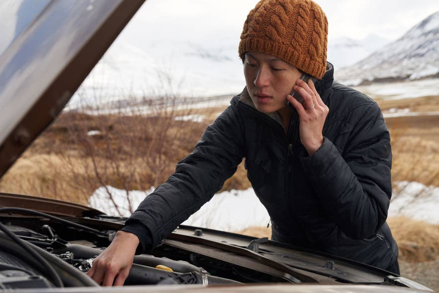 Woman using a mobile phone, with a stopped vehicle in Iceland.