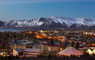 Ein Blick über Reykjavik bei Nacht mit schneebedeckten Bergen im Hintergrund.