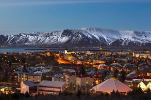 En vy över Reykjavik på natten med snötäckta berg i bakgrunden.