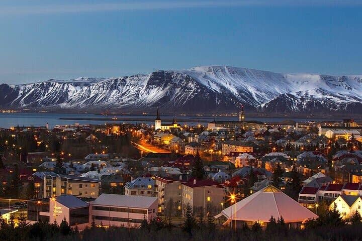 Utsikt over Reykjavik om natten med snødekte fjell i bakgrunnen.