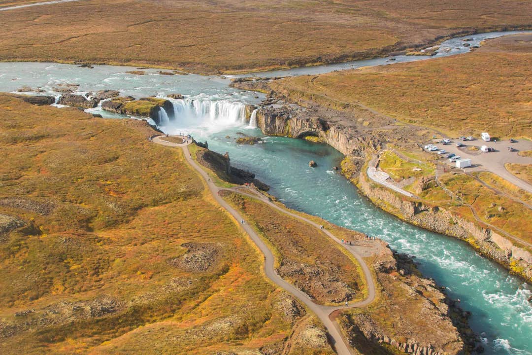 Aerial view of Godafoss Waterfall with walking paths, lookout points, and parking area surrounded by autumn-colored terrain.