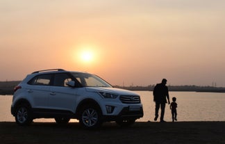 A person and a child watch the sunset beside a car.