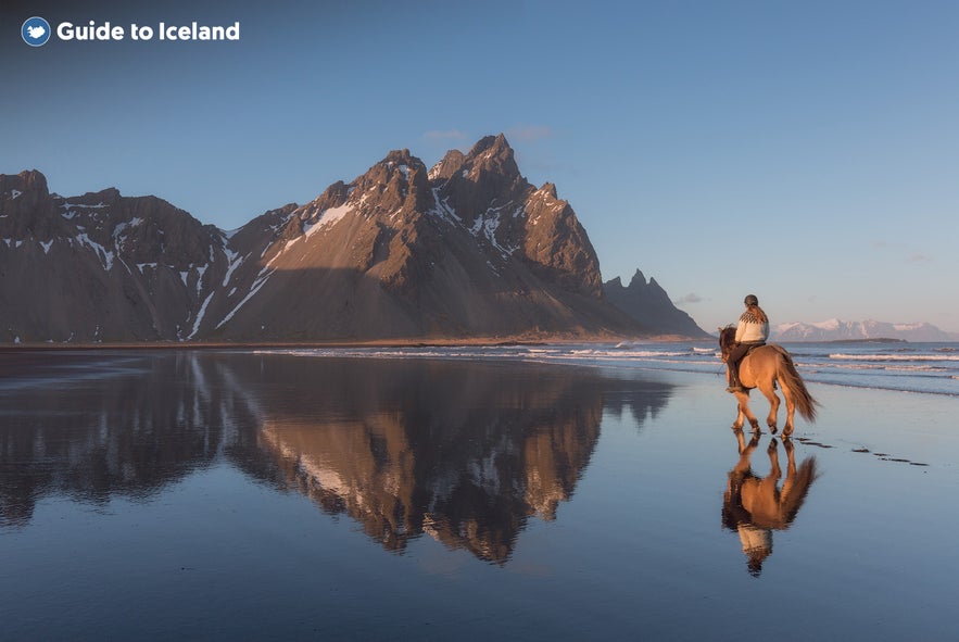 An adventurer riding a horse on the black sand beaches surrounding Mount Eystrahorn.