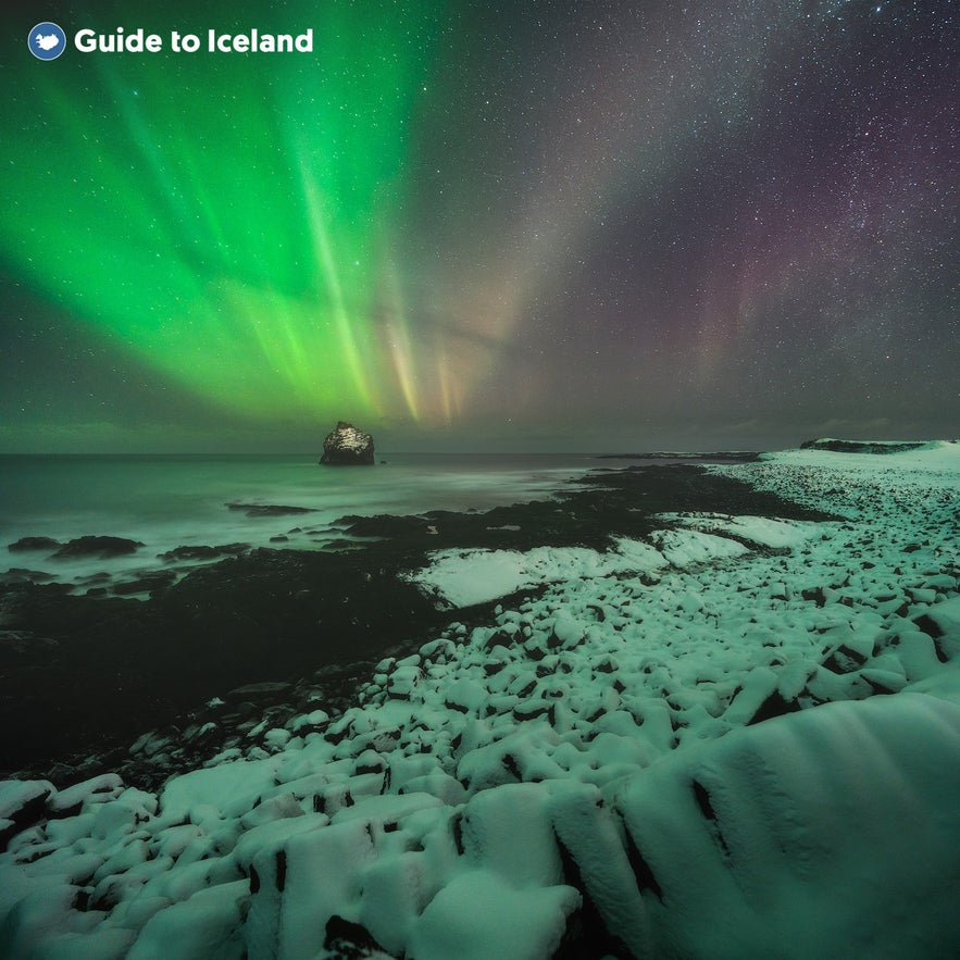 The northern lights glimmer over the snow-covered Reykjanes sea cliffs during winter.