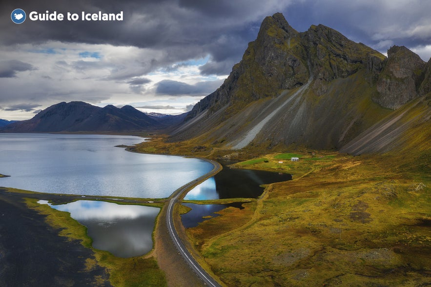 Mountains, beaches, and the ocean surround the Hvalnes lighthouse in Iceland.