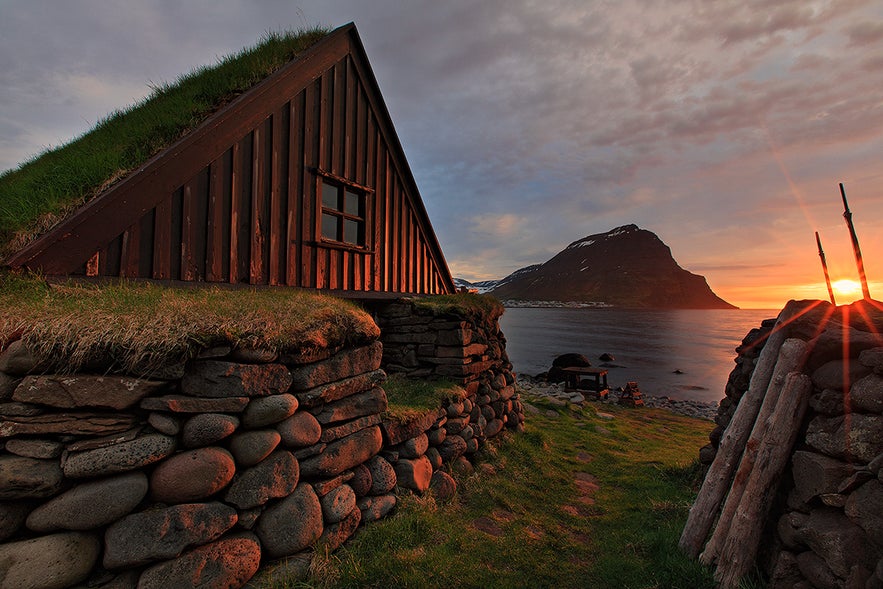 Sunset over a turf-roofed house by the sea near Isafjordur in Iceland’s Westfjords, with dramatic mountains and coastal views.