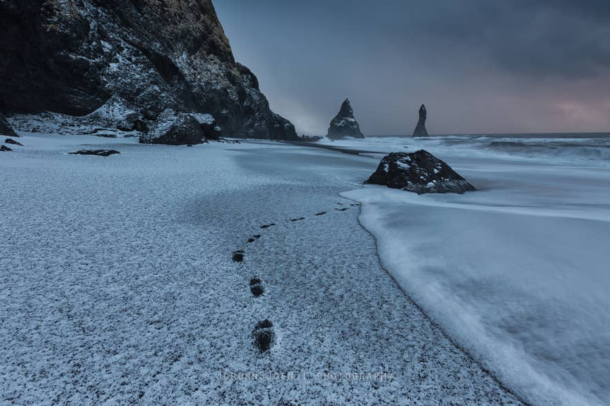 Snow-covered Reynisfjara Black Sand Beach and Reynisdrangar Sea Stacks near Vik under dark skies in December, Iceland's darkest month.