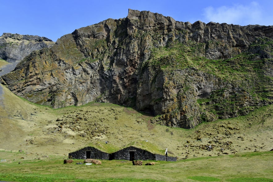 A view of Herjolfsdalur with its lush valley, surrounding mountains, and stone house.