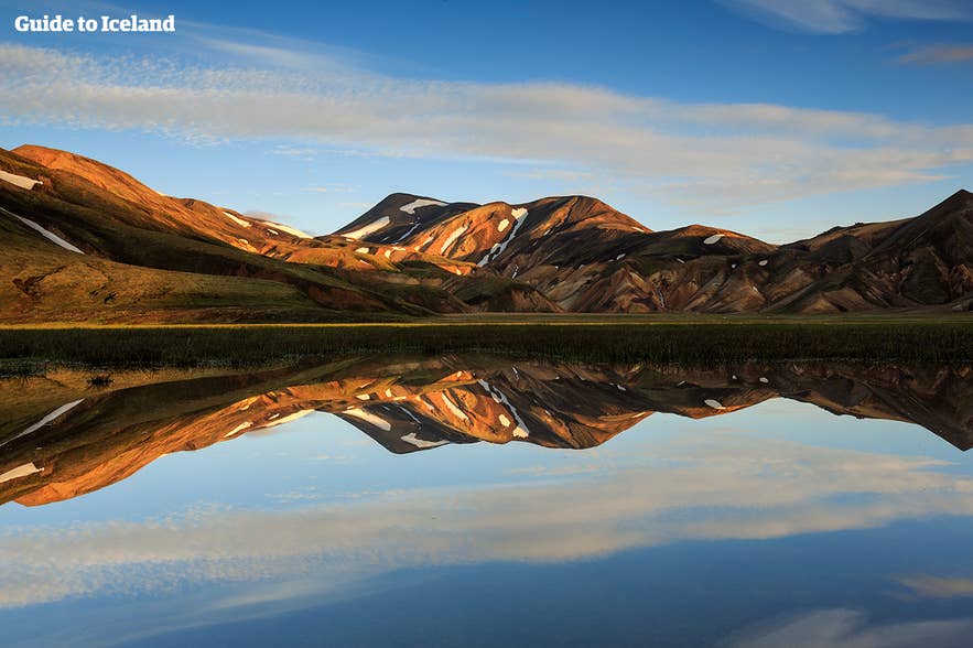 Landmannalaugar rhyolite mountains reflect in calm water at sunset, showcasing vivid colors during summer in Iceland.
